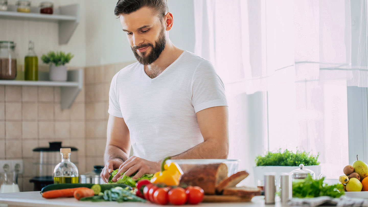 Një atlet mashkull po përgatit një vakt të shëndetshëm në kuzhinë.

